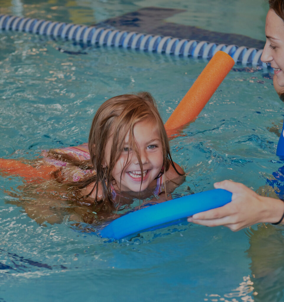 Young girl using pool noodles to swim, showcasing beginner tips for swimmers