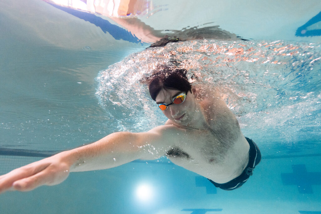 A swimmer underwater, performing a stroke during swimming lessons to improve technique and strength in an indoor pool