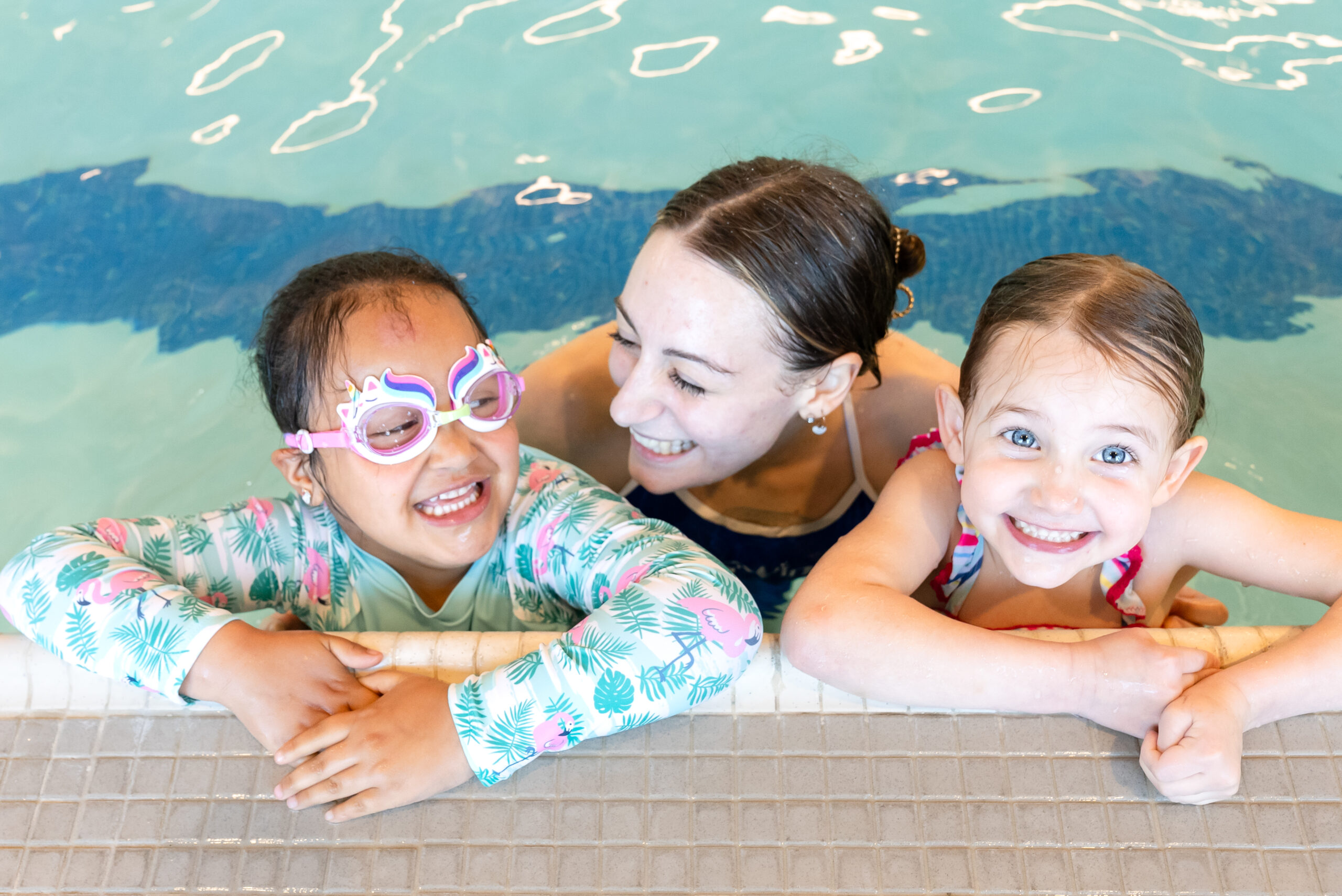 Two smiling children with swim goggles and their instructor during a swim class in Long Island