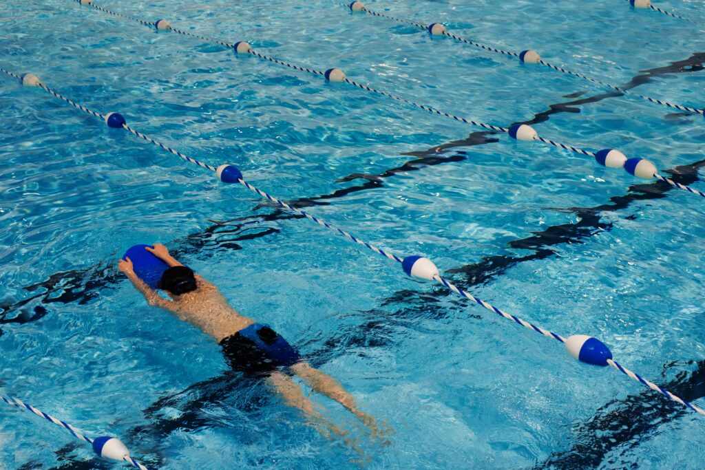 A person practicing with a kickboard during indoor swimming classes, improving their leg strength and swimming skills