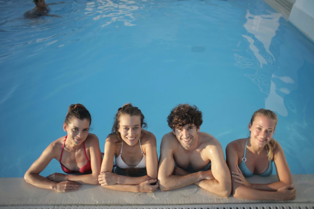 A group of four swimmers smiling and relaxing by the poolside after their indoor swimming class, highlighting the social aspect of swimming lessons