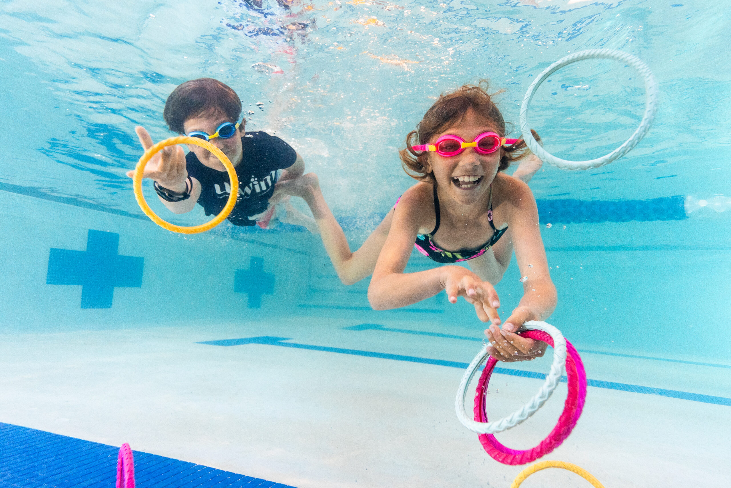 Two kids playing underwater with swim rings at swim school
